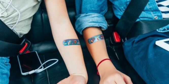 enfant assis dans une voiture avec des pansements de couleur sur les bras

